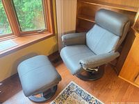 Full view of grey leather swivel recliner chair beside window with matching ottoman