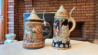 Front view of both steins showing relief scenes and pewter lids