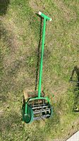 Full view of green manual lawn aerator laid on grass