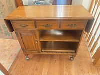 Front view of Roxton maple bar cart, leaves down, showing drawers, cabinet, shelf, casters