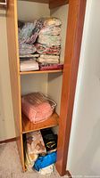 Tall narrow shelving unit holding multiple unopened packages of vintage bed linens including sheet sets, pillowcases, comforters