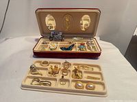 Overall view of red jewellery box and lower tray showing assortment of rings, brooches, earrings, pendant watch