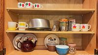 Cabinet shelves with Pyrex bowls, Fire-King mugs, recipe plates, teapot, metal tools
