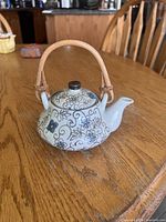 Full side view of porcelain teapot showing floral pattern and rattan handle