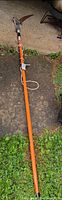 Full length view of orange fiberglass pole saw on ground
