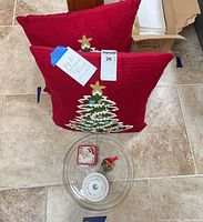 Two pillows, glass platter, candlestick, bell ornament, tin box arranged on floor