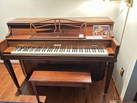 Front view of Baldwin upright piano with bench showing keyboard, music rack, pedals