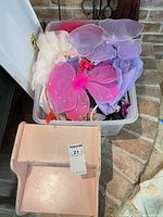 Clear bin with dress-up items and pink stool in foreground