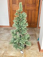 Full view of slim green artificial Christmas tree on tile floor