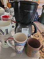 Coffee maker with glass carafe and six assorted ceramic mugs