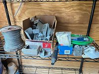 Overview of lot on shelf showing wire spool, box of metal parts, green cable, misc hardware