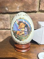 Front view of M.I. Hummel Umbrella Girl porcelain egg on wood stand