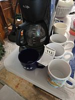 Coffee maker, carafe, and four mugs visible together