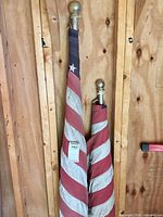 Two bundled US flags on poles leaning against wood wall; gold finials visible