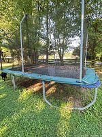 Full view of rectangular trampoline showing blue frame, green pad, safety net poles and damaged net
