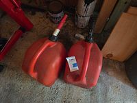 Two red plastic gas cans side by side on floor showing overall form and spouts