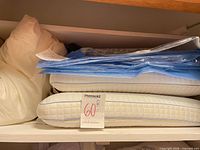 Stack of white quilted pillows and packaged blue vacuum bags on shelf