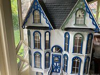 Front exterior of dollhouse showing white walls, blue and green trim, arched windows, shingled roof