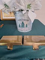 Bucket with FARM FRESH Christmas Trees graphic filled with white poinsettias; two gold stocking holders in front
