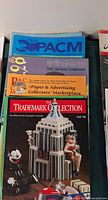 Stack of magazines showing PACM, The Tin Box Company, PACM orange issue, Trademark Collection