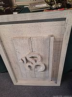 Front view showing framed distressed white wooden sign with raised centre panel and decorative scroll motif