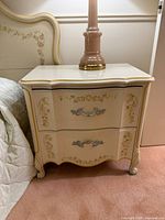Front view of one nightstand showing drawers, floral motifs, hardware, legs