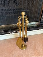 Full view of brass fireplace tool set on stand in front of fireplace