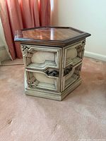 Front angle of hexagonal side table showing cream base, molded panels, metal hardware