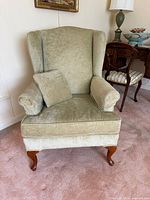 Front angled view of sage green velvet wingback armchair with accent pillow