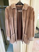 Front view of beige fur coat on hanger showing exterior, collar, pockets