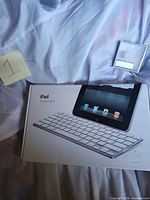 Sealed retail box of iPad Keyboard Dock and empty clear plastic iPod shuffle case visible