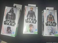 Front view of three boxed Star Wars figures – Darth Vader, Luke Skywalker, Bo-Katan