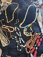 All necklaces laid out on dark fabric showing variety of colours, materials and strand styles