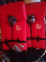 Front view of both red life jackets showing approval logo, straps and tags