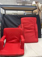 Front view showing both red folding stadium chairs, one upright with armrests, one flat back panel