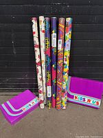 Six gift-wrap rolls and two Kids “R” Us boxes standing together