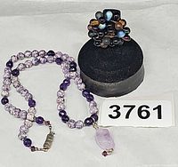 Necklace coiled beside cluster ring on stand showing lot contents and reference number