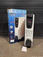 Heater standing beside original box, front view showing controls and cord storage