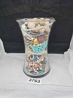 Glass vase filled with assorted costume jewelry pieces