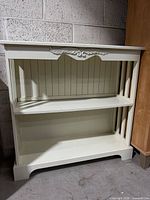 Front view of off-white painted wood bookcase showing shelves and decorative details