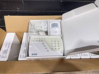 Open shipping cartons showing multiple boxed Orbic alarm kits and one opened inner box displaying control panel, motion sensor, cables and manuals.