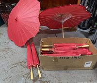 Box containing multiple folded red paper parasols with two shown opened upright