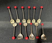 Twelve silver-plated cocktail spoons displayed bowl side up showing red bead finials.