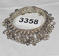 Full view of the hinged silver-tone charm bracelet showing overall design and number tag