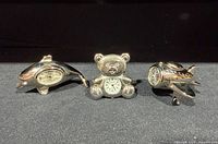 Front view of all three silver novelty desk clocks: dolphin, teddy bear, jet