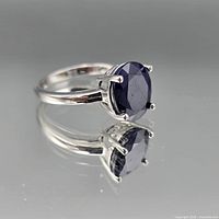 Ring side view showing oval blue stone in four prongs and reflection