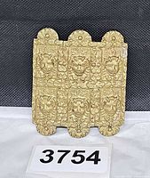 Front view of brass buckle showing nine embossed mask panels and floral motifs