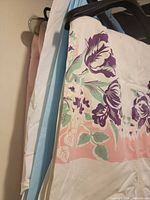 White tablecloth with purple floral print and other cloths hanging behind