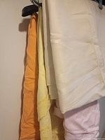 Four folded pastel tablecloths hanging: peach, yellow, ivory, pink