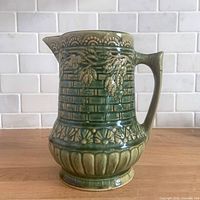 Front view showing green glazed pitcher with embossed roses and basketweave